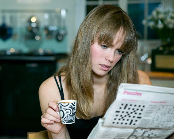 Person solving a crossword puzzle with
a coffee cup on the table, searching for the
Phil or Lil of Rugrats crossword clue answer