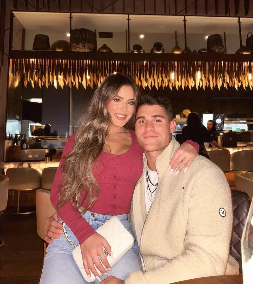 Billy Seidl and his fiancée Brielle Biermann smiling together inside a restaurant.