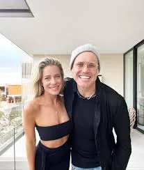 Chef Brian Malarkey smiling in a black shirt and grey beanie next to Danielle Harley on a balcony.