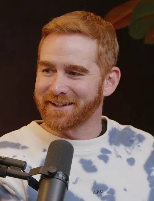 Andrew Santino smiling in front of a studio microphone during a podcast taping